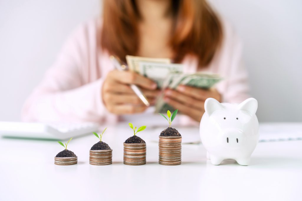 Young woman calculating expenses with stack of coins and piggy bank, Saving money for future investment concept