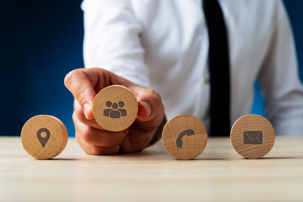 Business customer service representative placing four wooden cut circles with contact and information icons on them in a row.