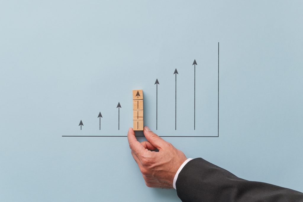 Business economy growth prediction graph - businessman making a chart with upwards pointing arrows. Over blue background.
