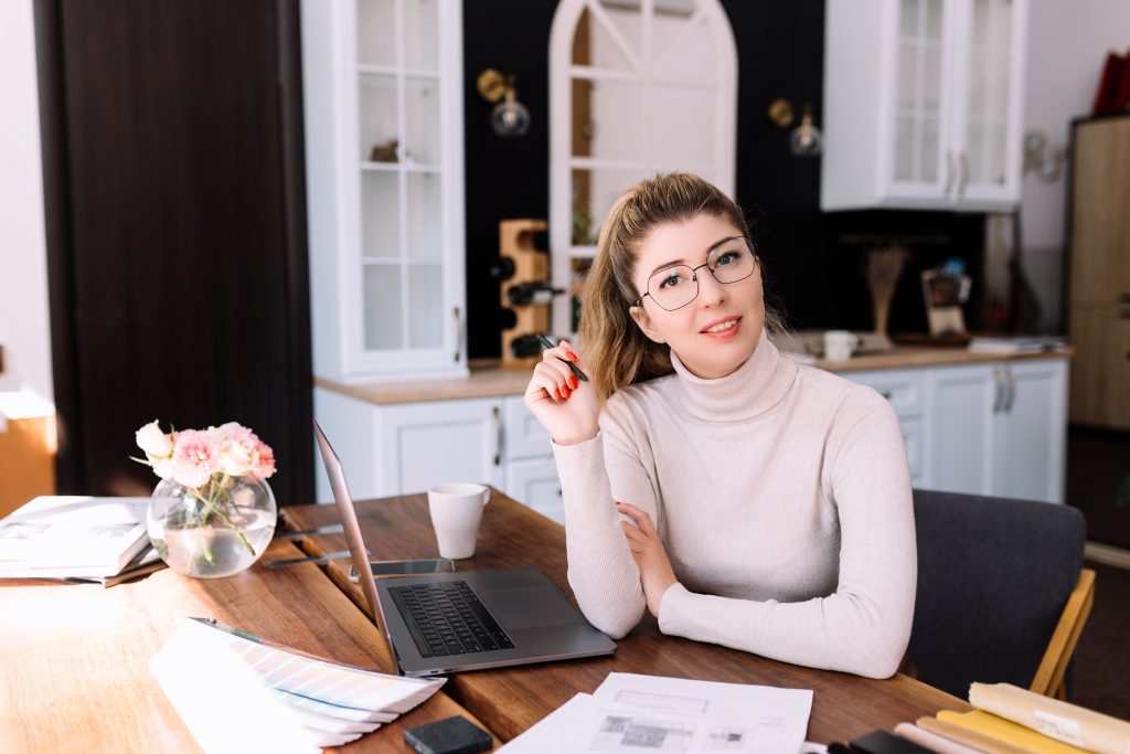 An interior designer is working on a new project, woman holding paper plan with pen. Considering the decision. Laptop on the desk. Thinking about new design. High quality photo