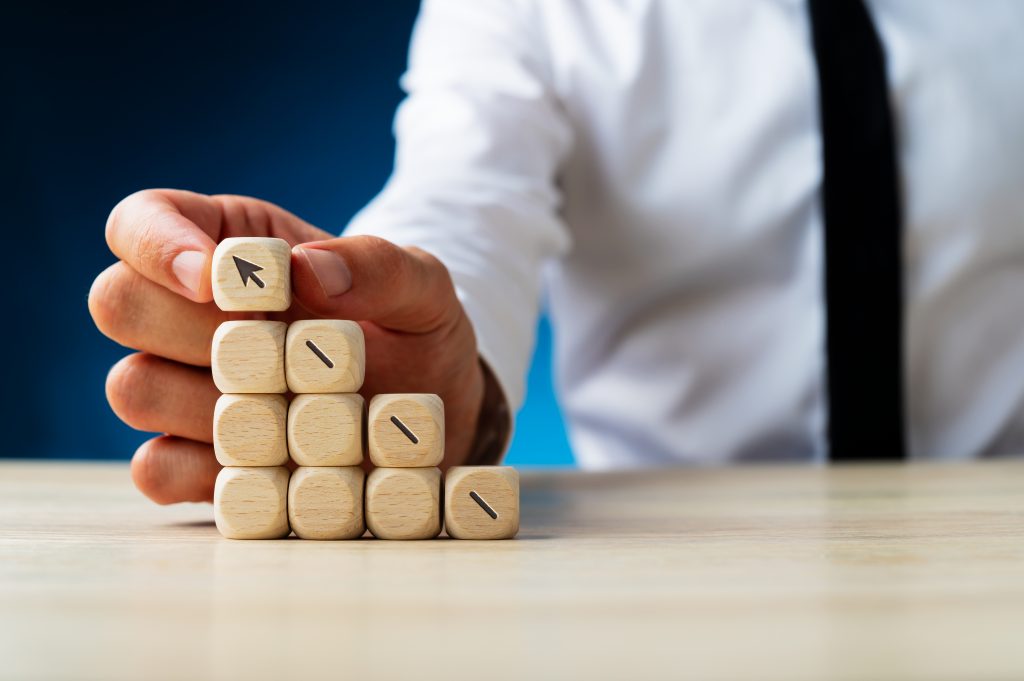 Businessman making a stack of wooden dices assembling an arrow shooting upwards in a conceptual image. Over navy blue background.