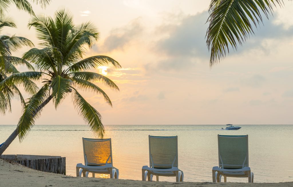 Sunrise over the ocean on dream beach vacation with palmtrees and deckchairs