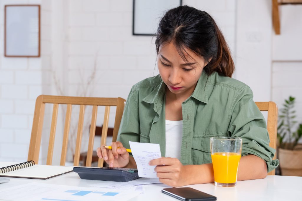 Asian woman use laptop and calculator calculate home budget in kitchen at home