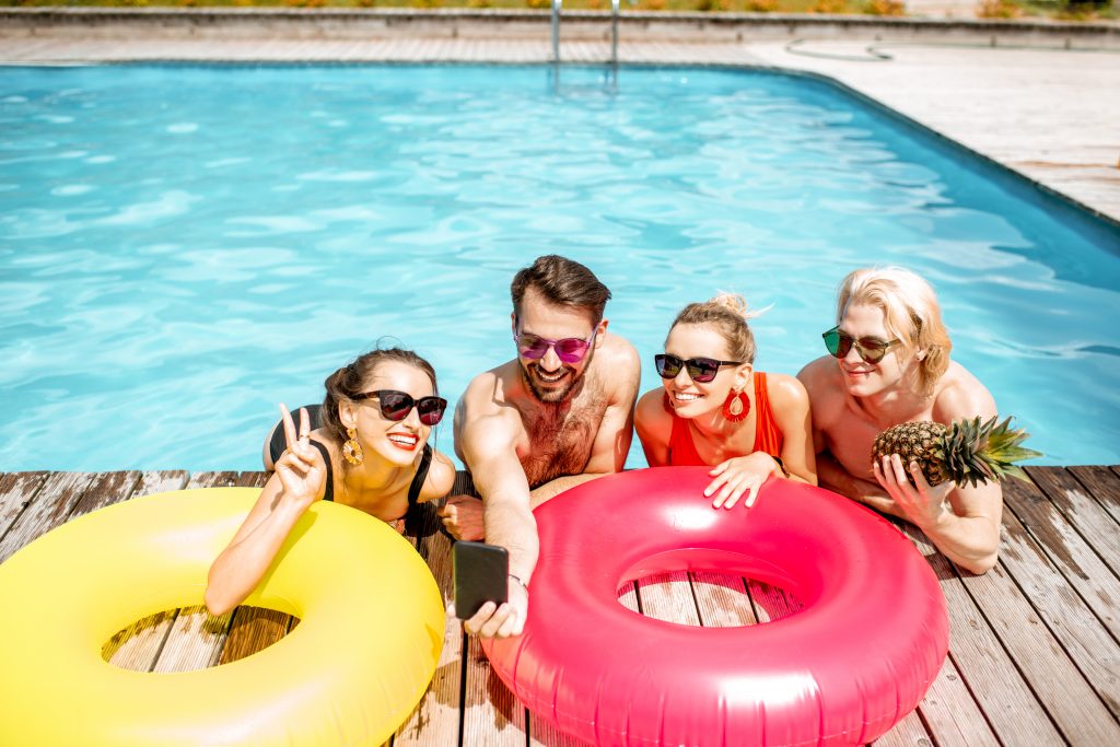 Group of a happy friends making selfie photo with inflatable rings, while having fun on the swimming pool outdoors during the summertime