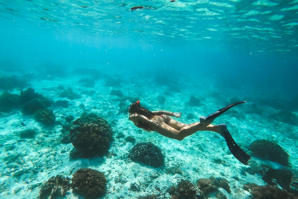 Woman snorkelling underwater with snorkel mask in clear transparent water in beautiful tropical lagoon with coral reef. Freediving activity. Leisure on vacations.