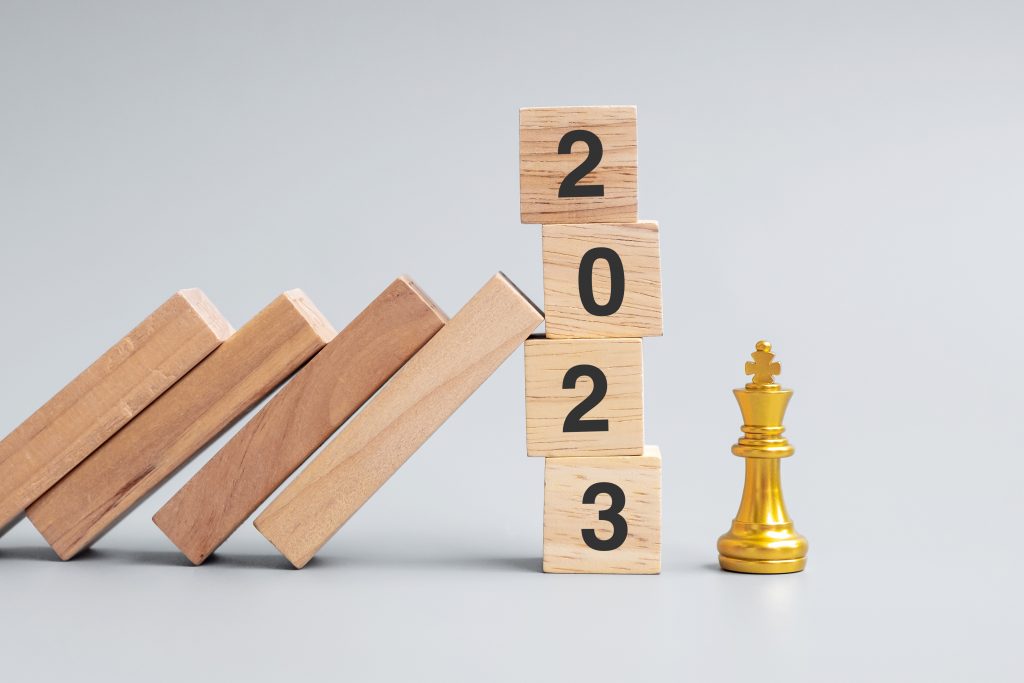 wooden Dominoes falling against 2023 stop blocks with golden Chess King figure. Business, Risk Management, Solution, economic, Insurance and New Year concept