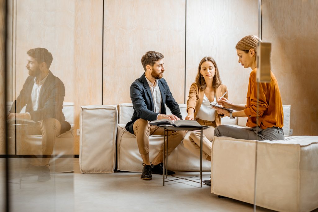Young couple talking with a sales manager or real estate agent, sitting on the comfortable couch in the office