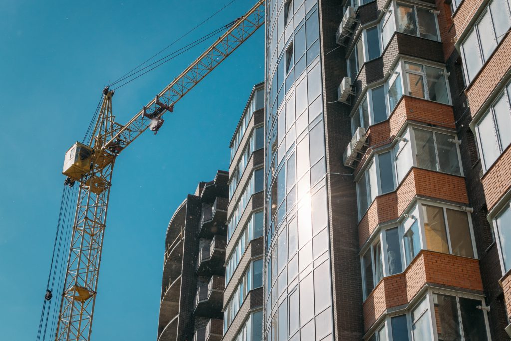 Building under construction and construction crane against blue sky and bright sun on summer day. Bottom view.