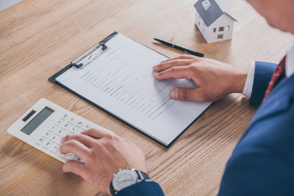 cropped view of businessman reading property management agreement and using calculator