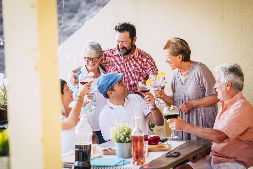 Group of multi generation friends and family having fun together during lunch at terrace. Group of people holding wine glass for toast. Family celebrating while having food and drinks