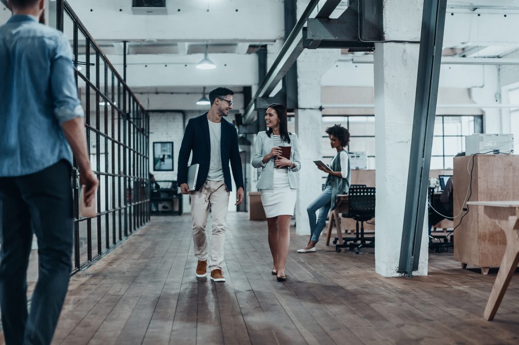 Pair of professionals. Full length of two young colleagues in smart casual wear discussing business and smiling while walking through the office corridor