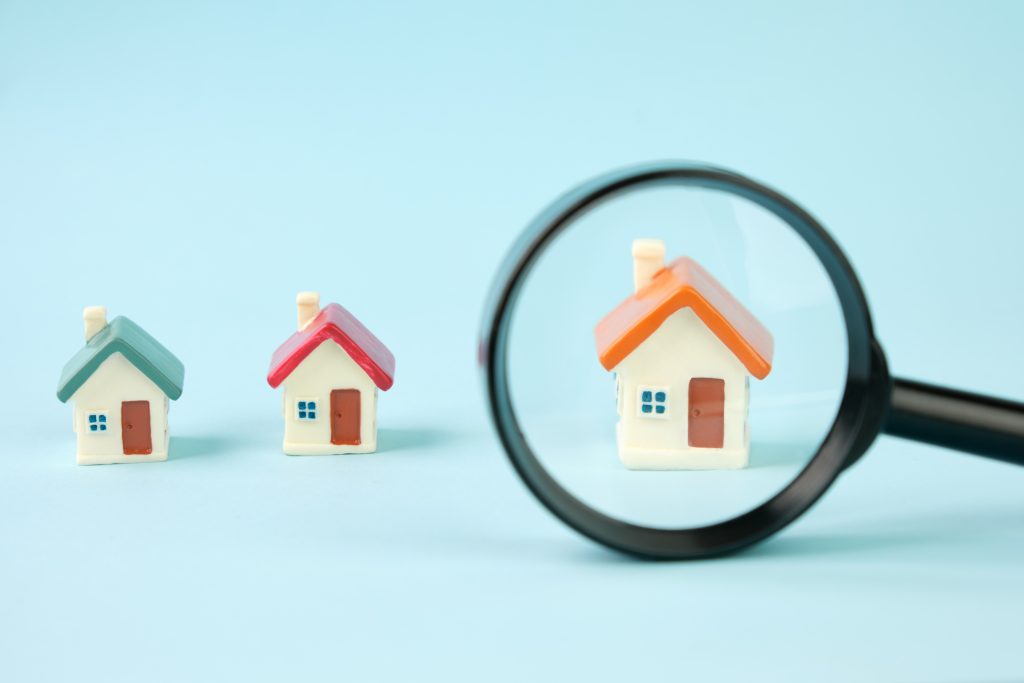 Small houses under a magnifying glass. Real estate search concept, purchase and sale of housing, rent, insurance.
