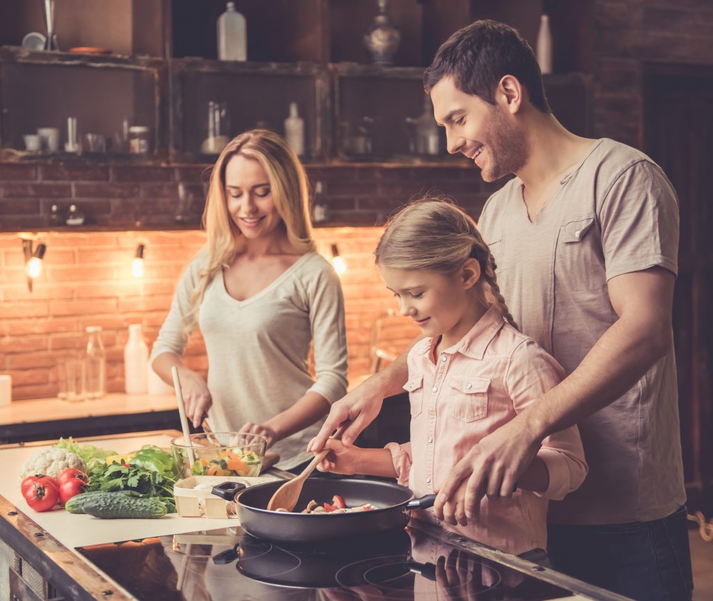 Cute little girl and her beautiful parents are  smiling while cooking in kitchen at home