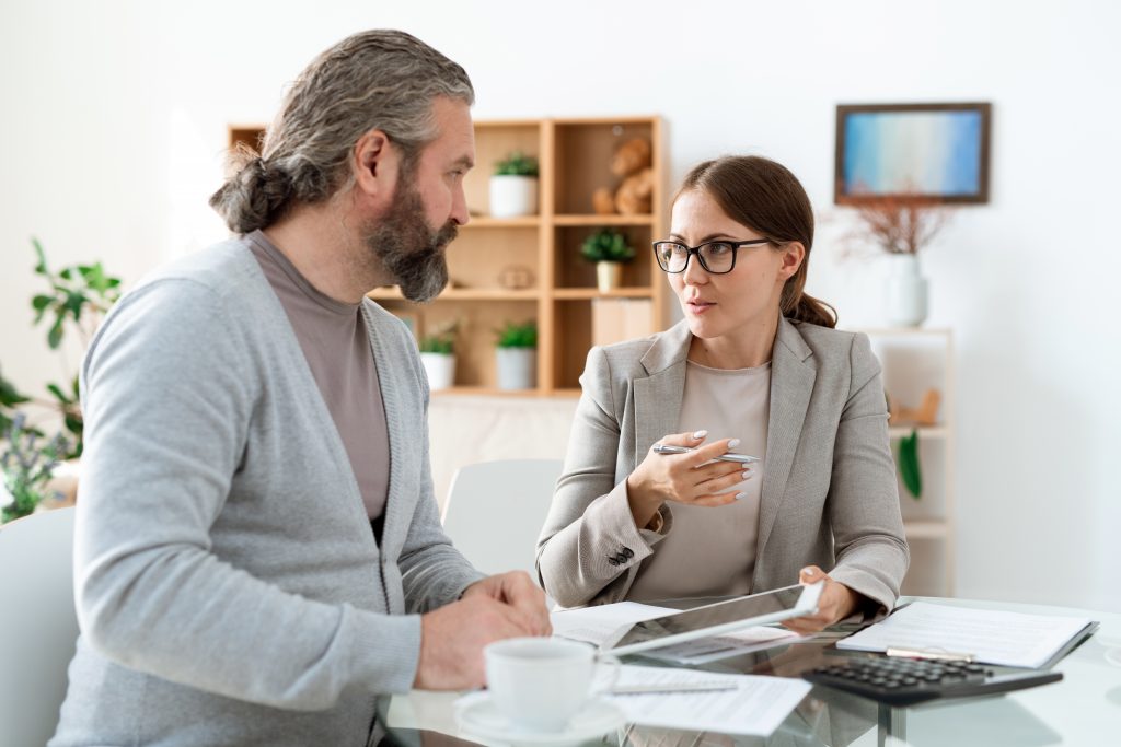 Young real estate agent with touchpad sitting next to her client while explaining him terms of deal
