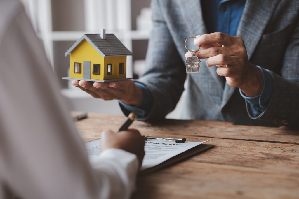 A home rental company employee is handing the house keys to a customer who has agreed to sign a rental contract, explaining the details and terms of the rental. Home and real estate rental ideas.