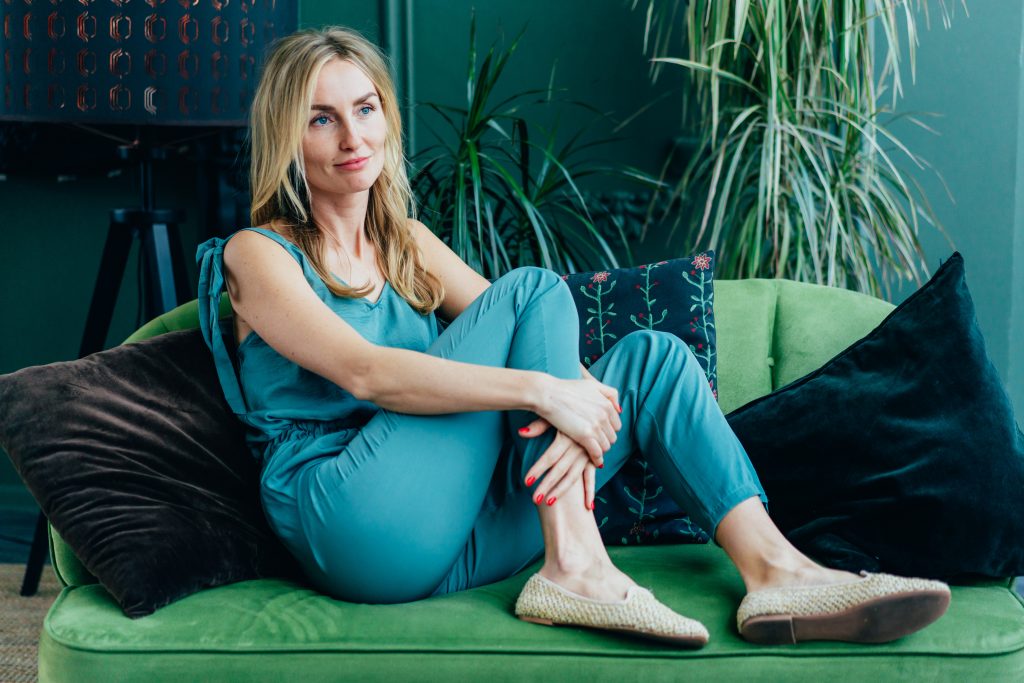 A woman in overalls is sitting on a green sofa. Portrait of a young adult millennial girl. Rest and privacy at home.