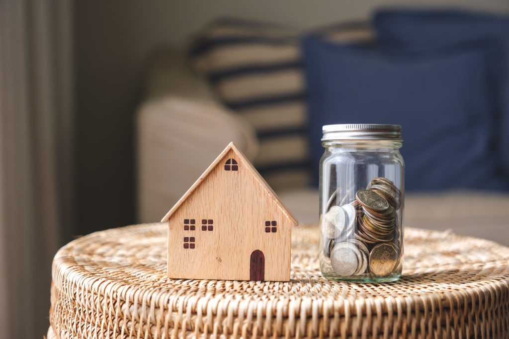 A wooden house model and a glass jar of coins for saving money concept