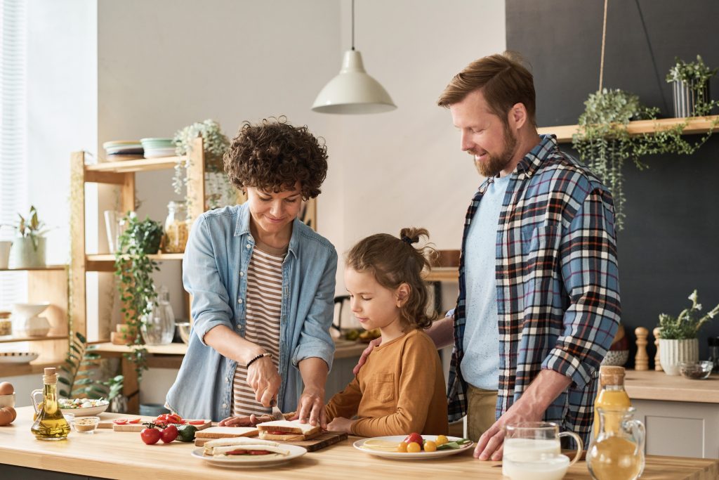 Family of three standing in kitchen and preparing sandwiches together with child