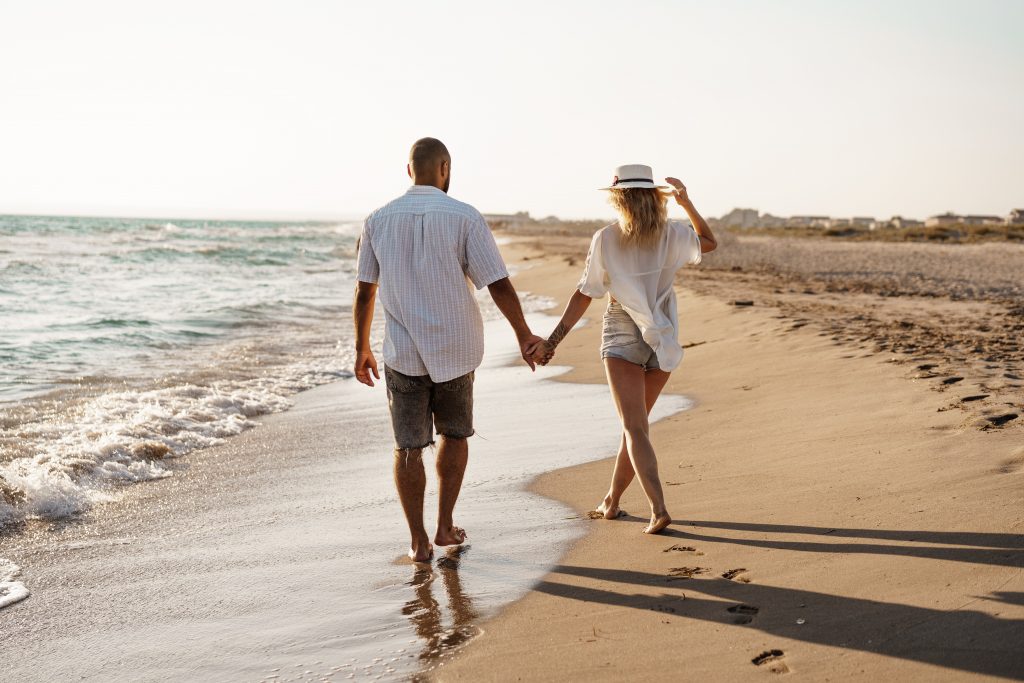 Young beautiful couple walking on beach near sea at sunset