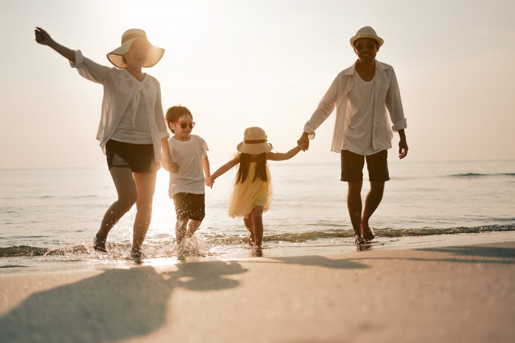 Asian family vacation holiday, Happy family running on the beach in the evening. Back view of a happy family on a tropical beach and a car on the side. Mother, father, children on the sea at sunset.