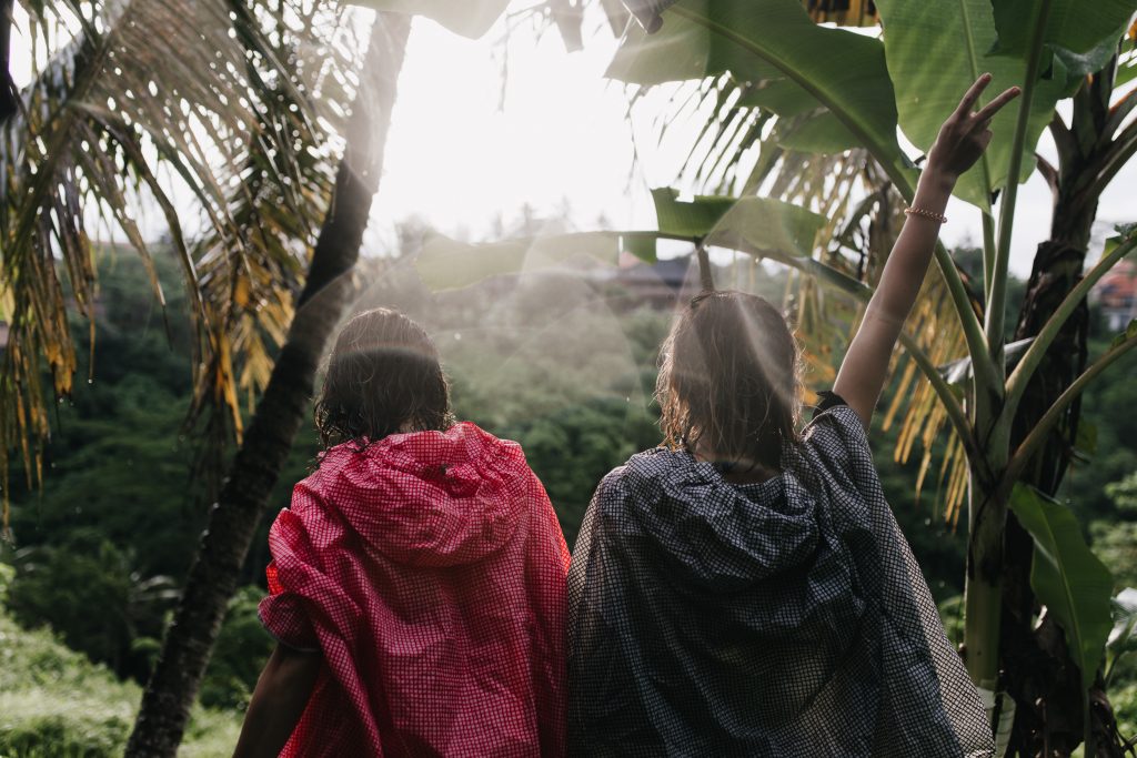 Brunette girl in pink raincoat exploring jungle with friend. Female tourists chilling during trip around exotic country.