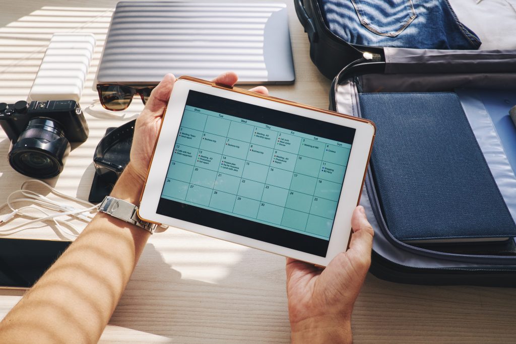Hands of traveler holding digital tablet with calendar on the screen