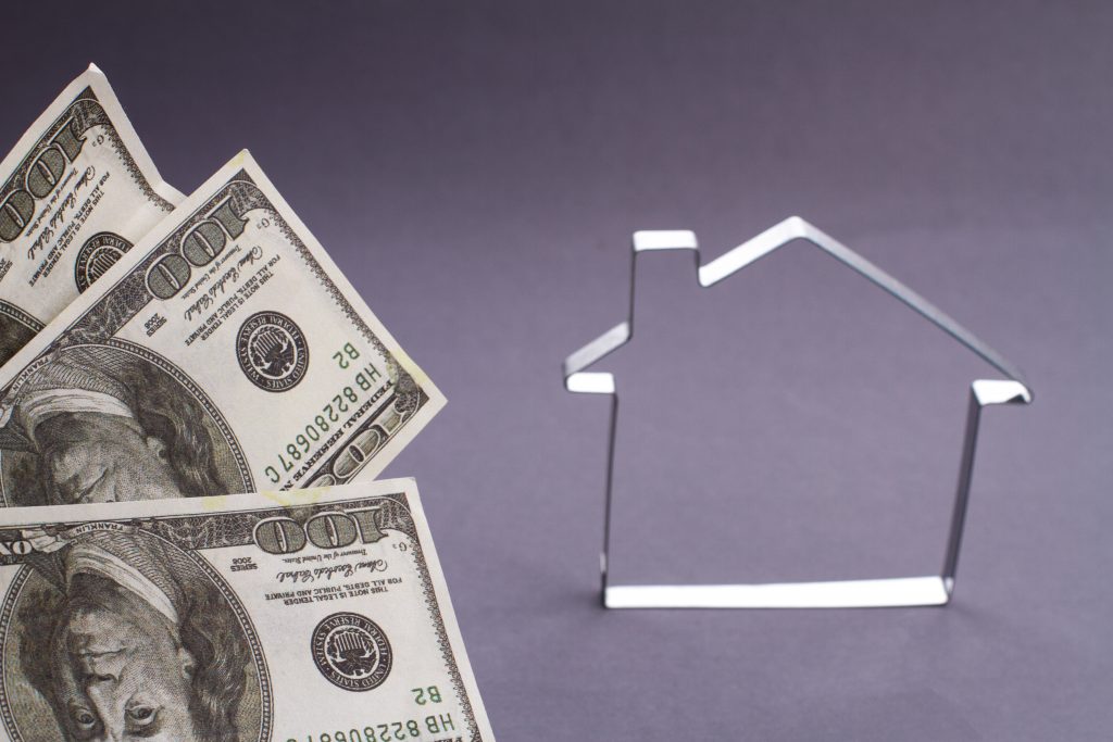 Concept investment in property. Metallic house outline frame and fan of dollars on grey background.