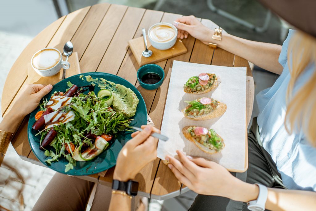 Women eating healthy vegetarian food at the cafe, close-up view from above on the table