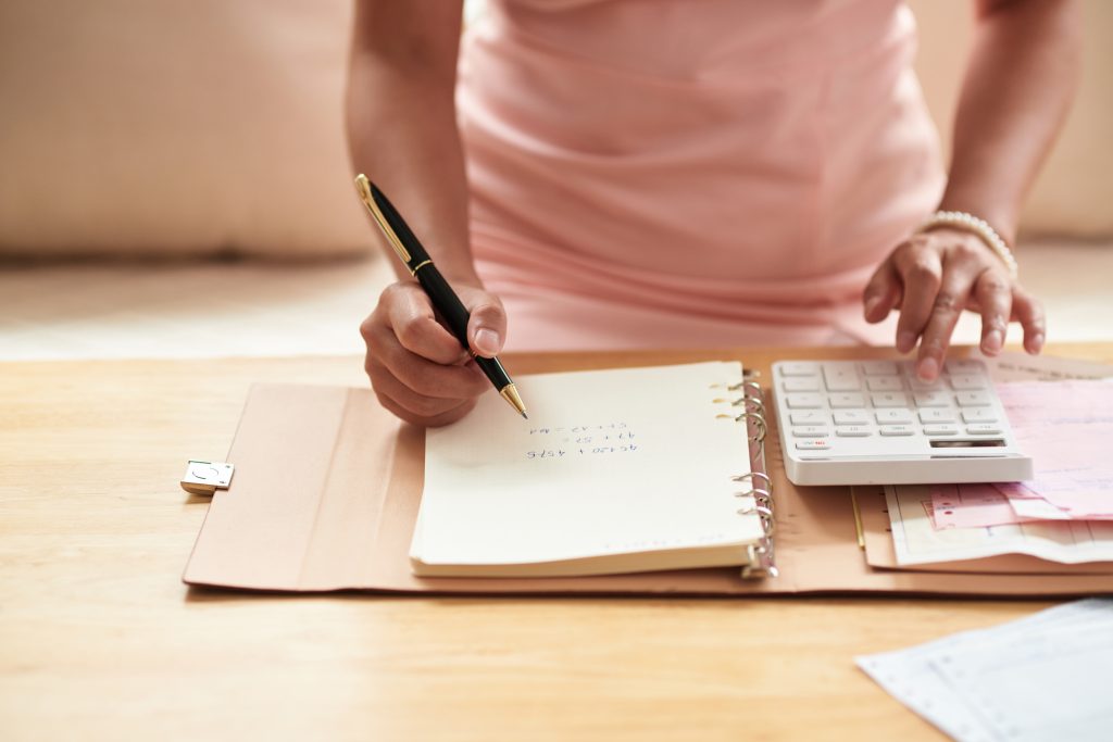 Close-up of young woman making notes in notepad and using calculator, she planning home budget