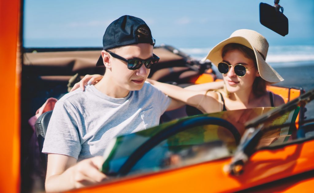 Young couple in casual clothes sitting in car with map embracing each other while choosing way of trip during summer holidays