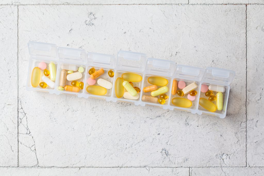Pills box for daily intake of vitamins and medicines, top view. Different capsules and tablets in a white container. Lifestyle for beauty and health.