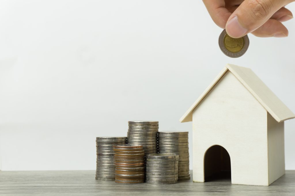 Saving money, home loan, mortgage, a property investment for future concept. A man hand putting coin over small residence house and money bag on white background and space. A sustainable investment.