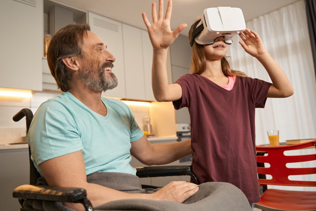 Happy disabled father watches his daughter immersed in virtual reality via gadget