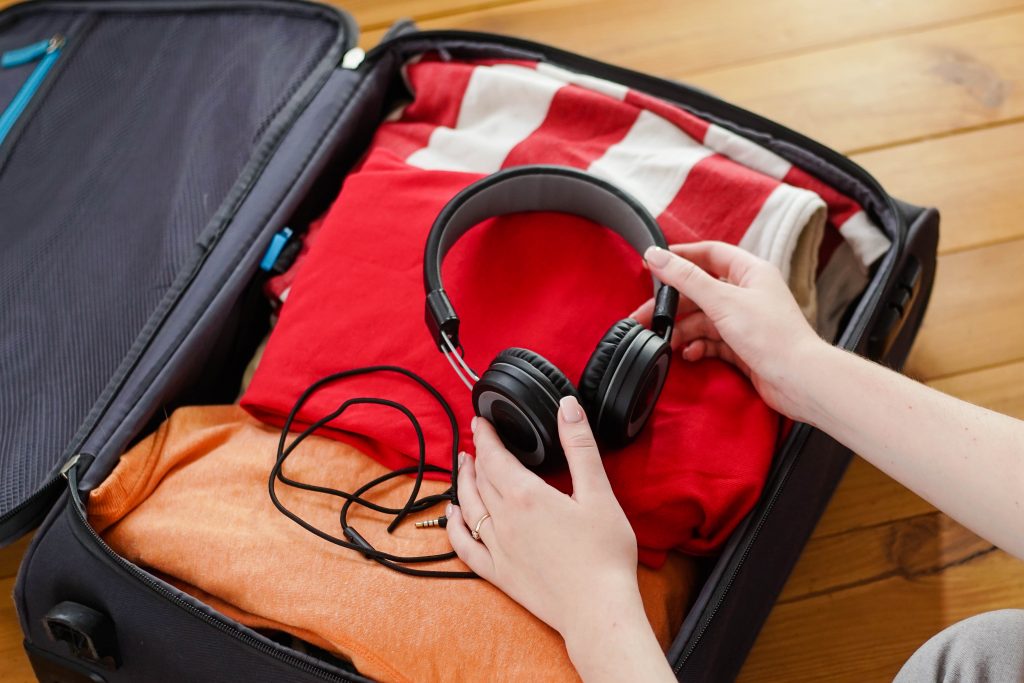 Woman put black headphones in a suitcase with clothes for vacation. Travel concept.