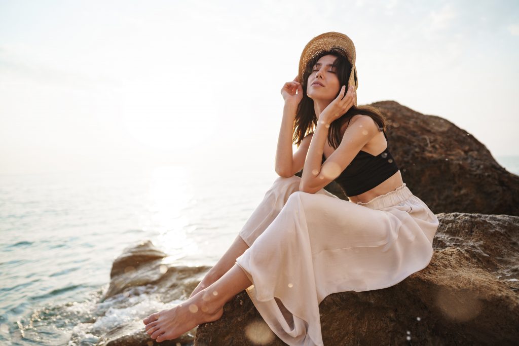 Woman traveler sitting near sea on cliff injoying view of sea and nature at summer