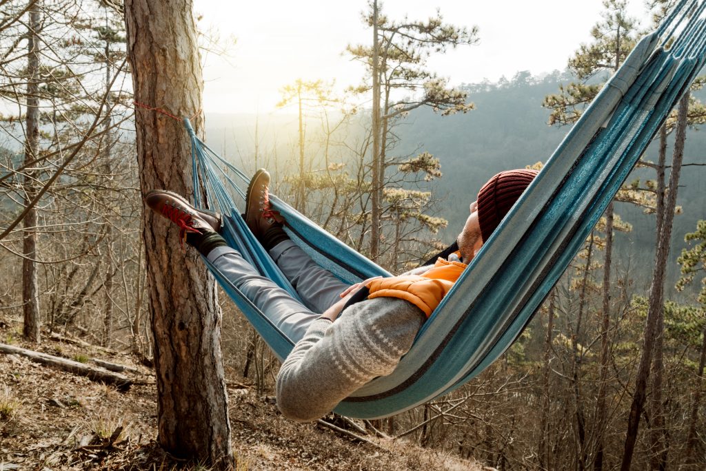 Young happy man relaxing lying in hammock on top of mountain.