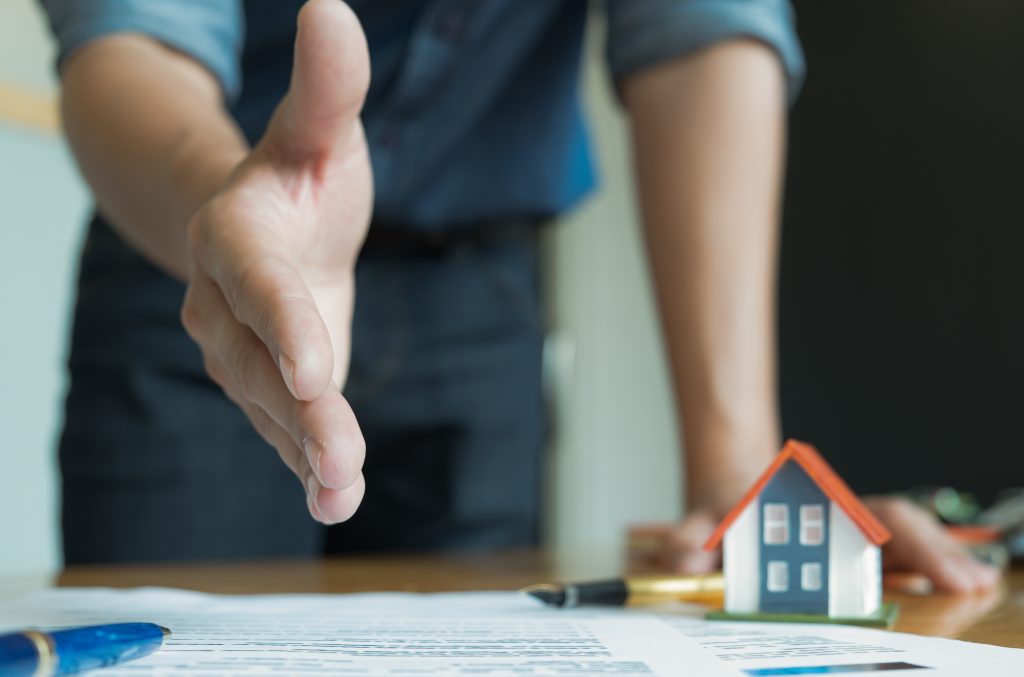 House sales staff extended their hands in front. Join hands with customers to close sales.Model houses and documents placed on the table.
