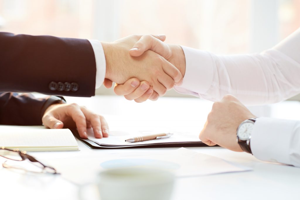 Close-up of unrecognizable businessman sitting at table and handshaking with new investor after signing contract