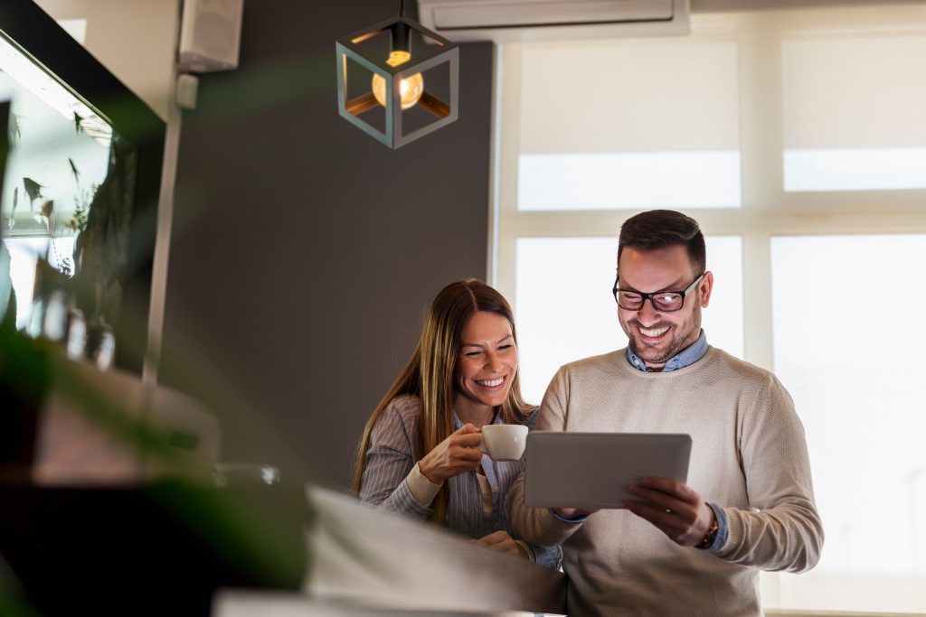 Beautiful young couple standing next to a bar counter, drinking coffee and using a tablet computer