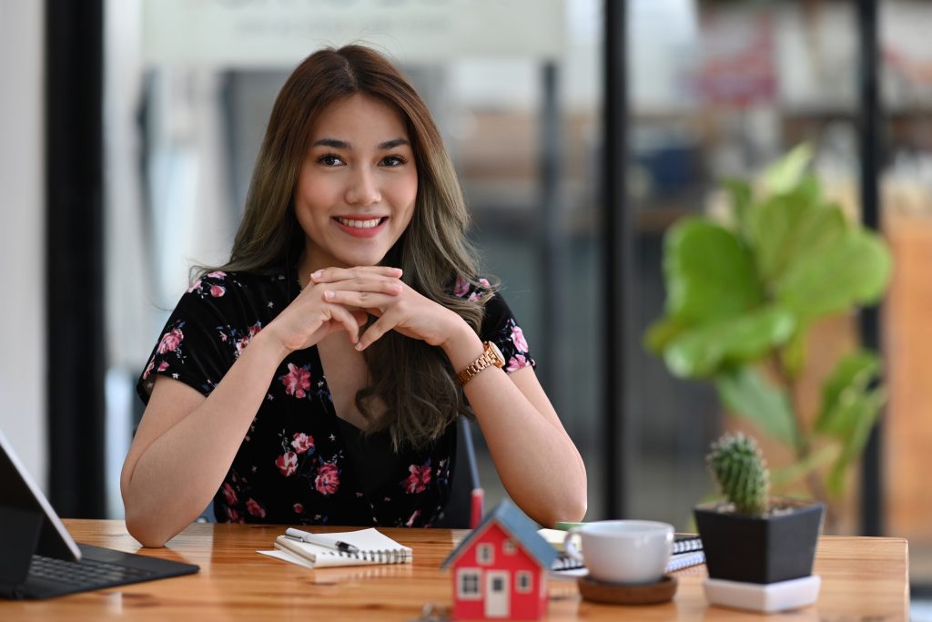 Attractive real estate agent woman sitting at her workplace and smiling to camera.