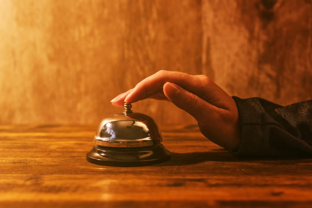 Businesswoman ringing hotel reception bell, warm retro toned image with selective focus