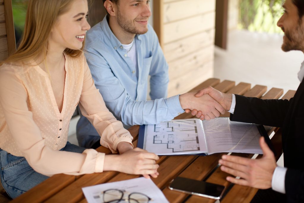 Real estate agent and clients shaking hands after signing property agreement, panorama